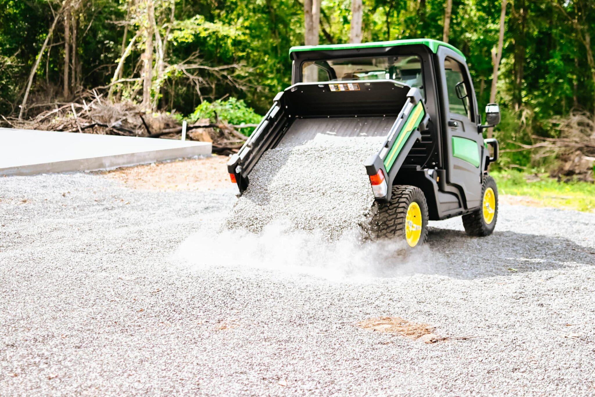 A John Deere Gator dumps gravel in a lot