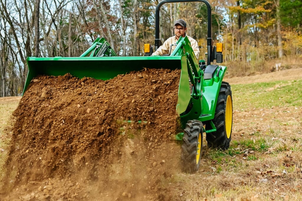 A person dumps dirt out of a John Deere tractor loader.