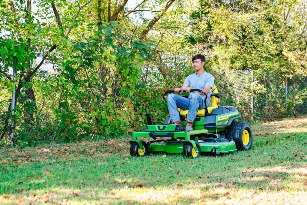 A man drives a John Deere zero turn mower