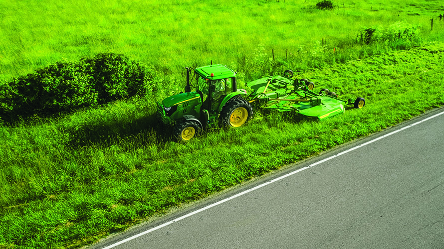 John Deere 6M tractor mows grass on a roadside