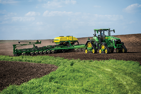 A John Deere 8RX row crop agriculture tractor pulls a planter in a farm field
