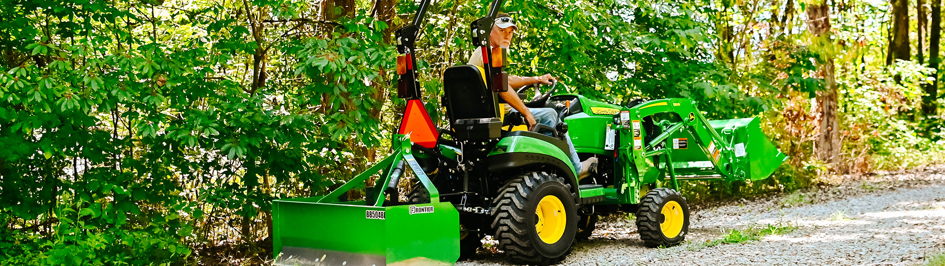 A man grades a driveway with a John Deere tractor package with box blade