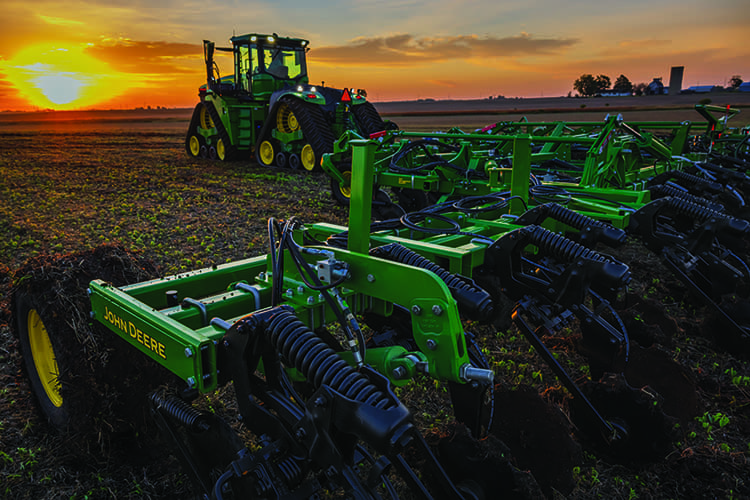 A John Deere tractor and nutrient applicator toolbar in a farm field at sunset.