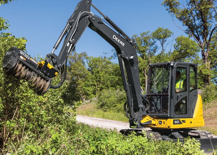A John Deere compact construction mini ex trims brush alongside a road