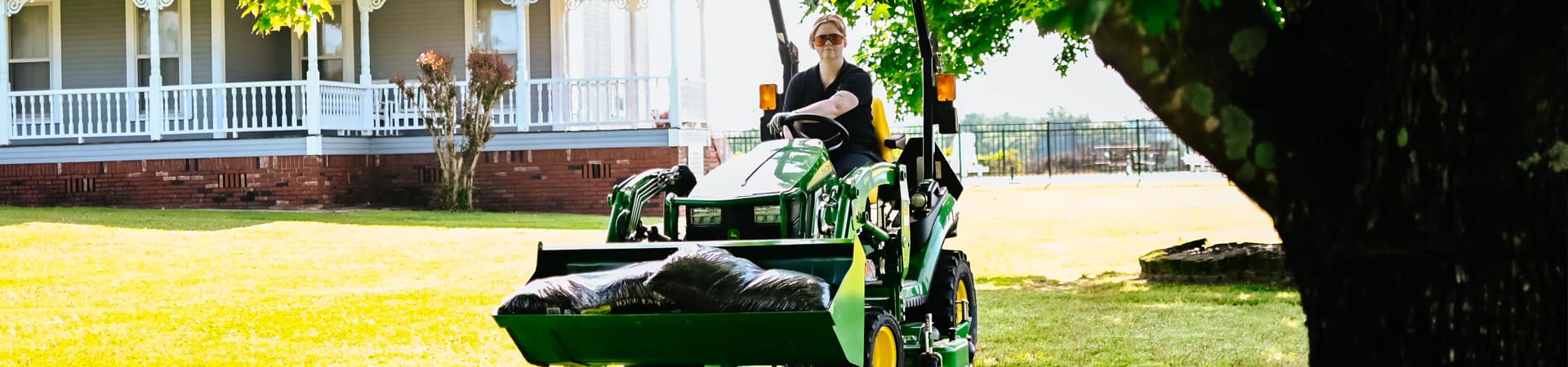 A woman moves mulch with a John Deere 1025R compact tractor loader
