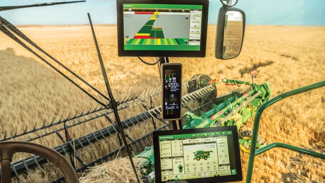 Inside the cab of a John Deere combine with precision agriculture displays at harvest