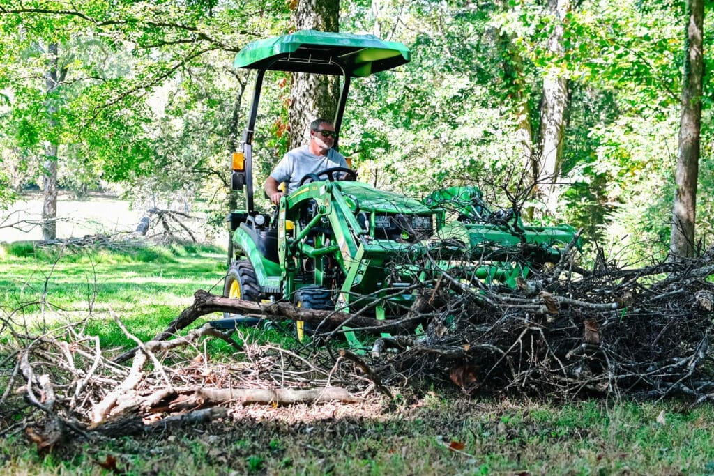 A person moves tree debris with a Deere 1025R and grapple