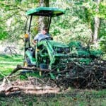 A person moves tree debris with a Deere 1025R and grapple