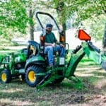 A person digs with a John Deere 1025R tractor and backhoe