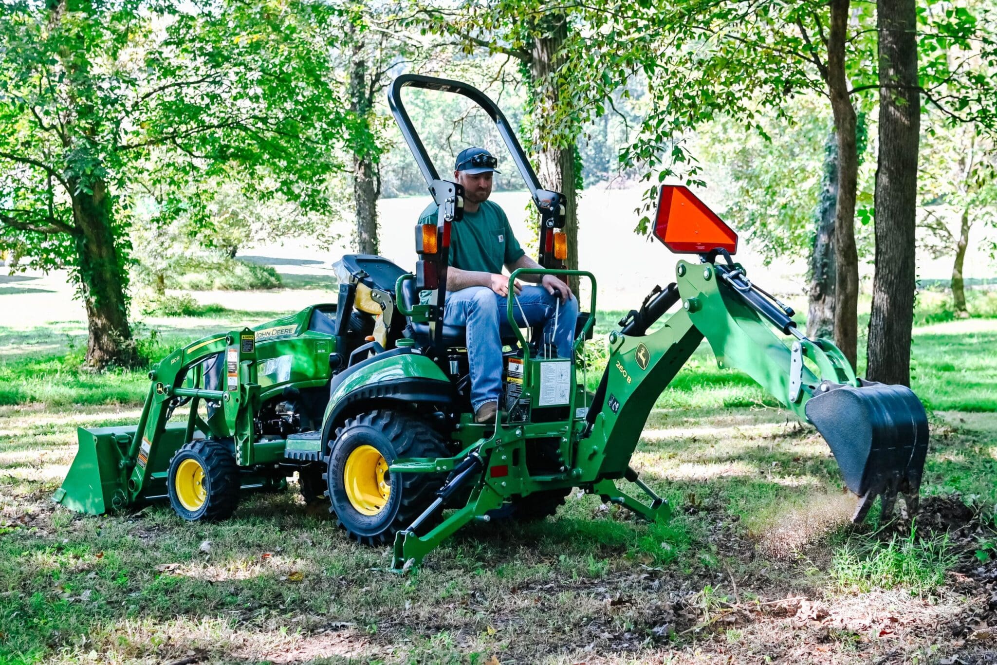 A person digs with a John Deere 1025R tractor and backhoe