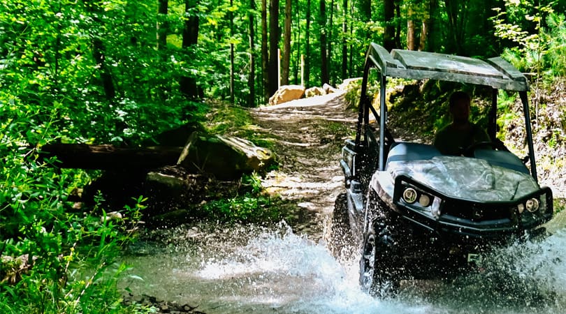 John Deere Gator side by side splashes through a creek