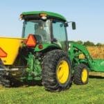 A John Deere 4066R with seed spreader next to a field