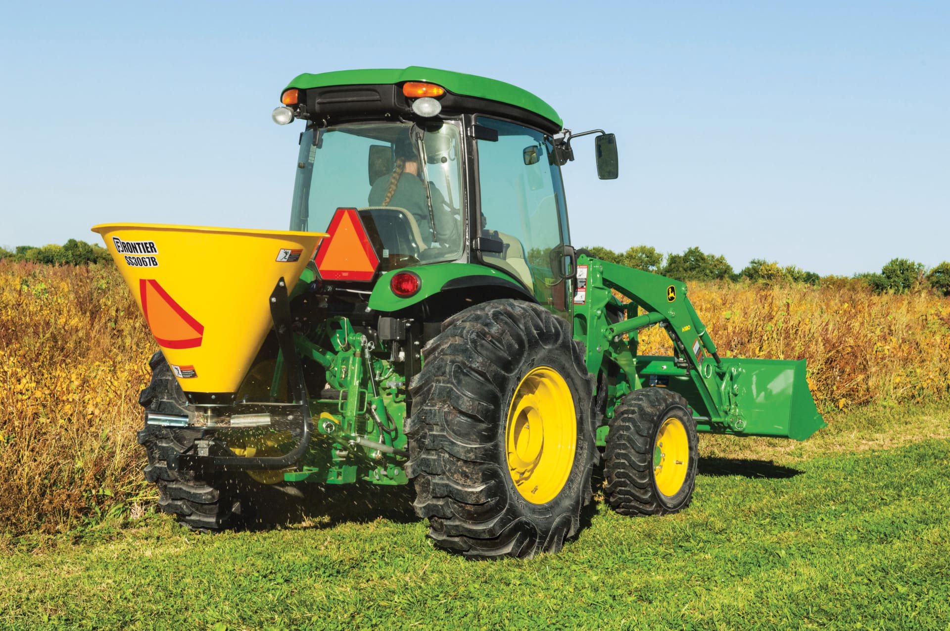 A John Deere 4066R with seed spreader next to a field