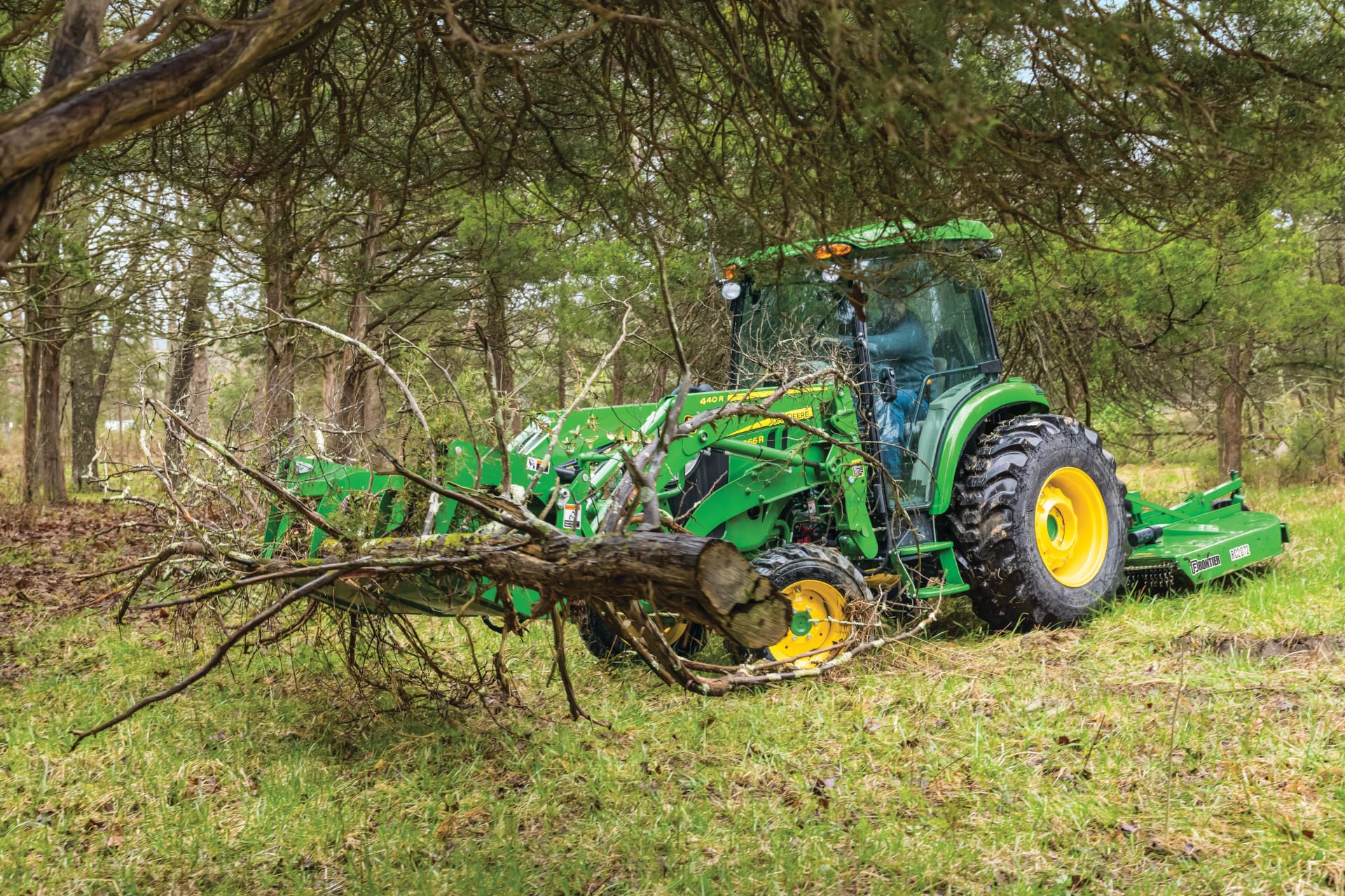 A John Deere 4066R tractor moves brush with a grapple