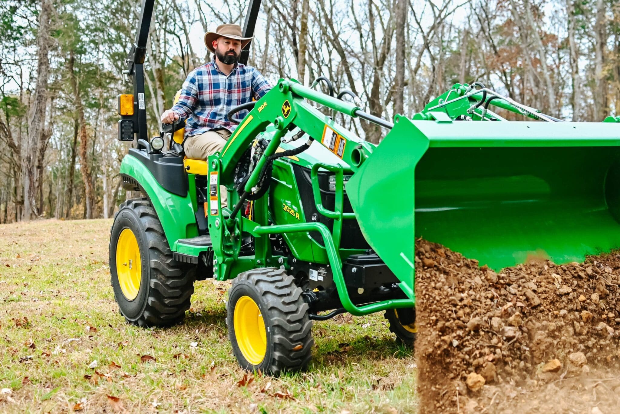 A person moves dirt with a John Deere 2R tractor and loader