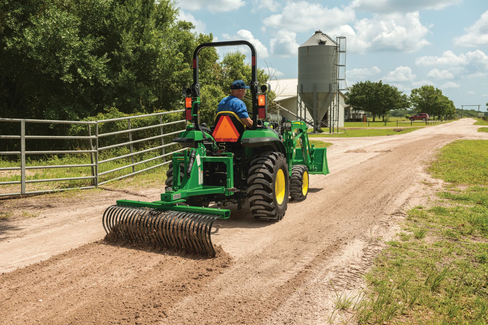 A person repairs a road with a John Deere small tractor