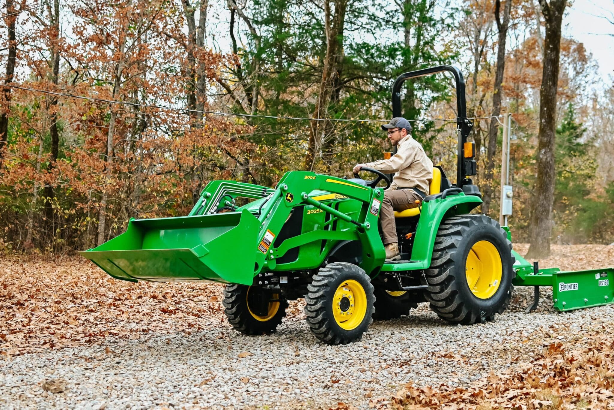 A man grades a driveway with a John Deere 3025E tractor and land plane