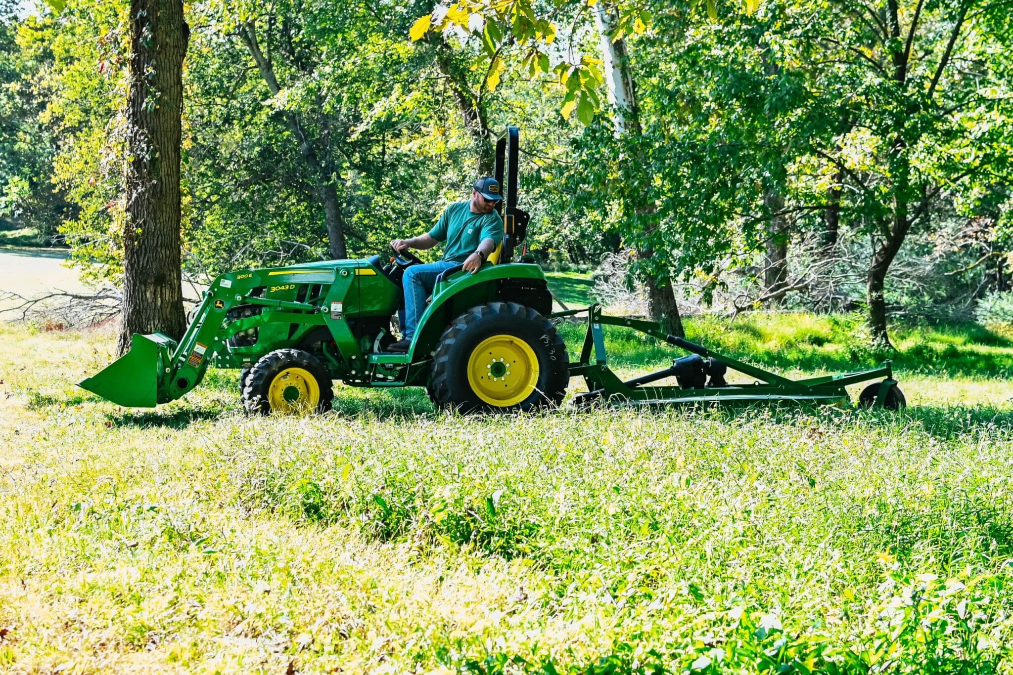 A man bush hogs with a John Deere 3043D tractor