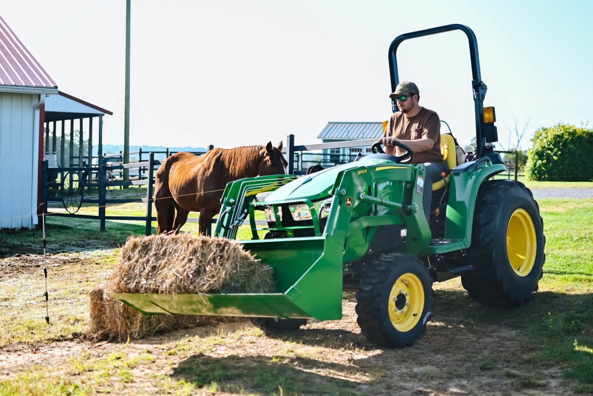 A man moves hay into a horse pasture with a John Deere 3E tractor