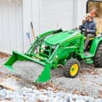 A man moves gravel with a John Deere 3R tractor loader