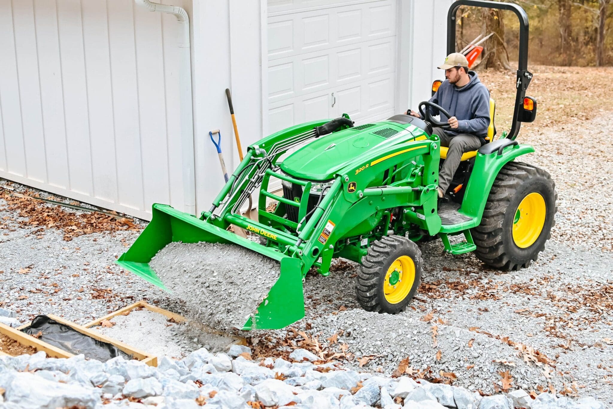 A man moves gravel with a John Deere 3R tractor loader