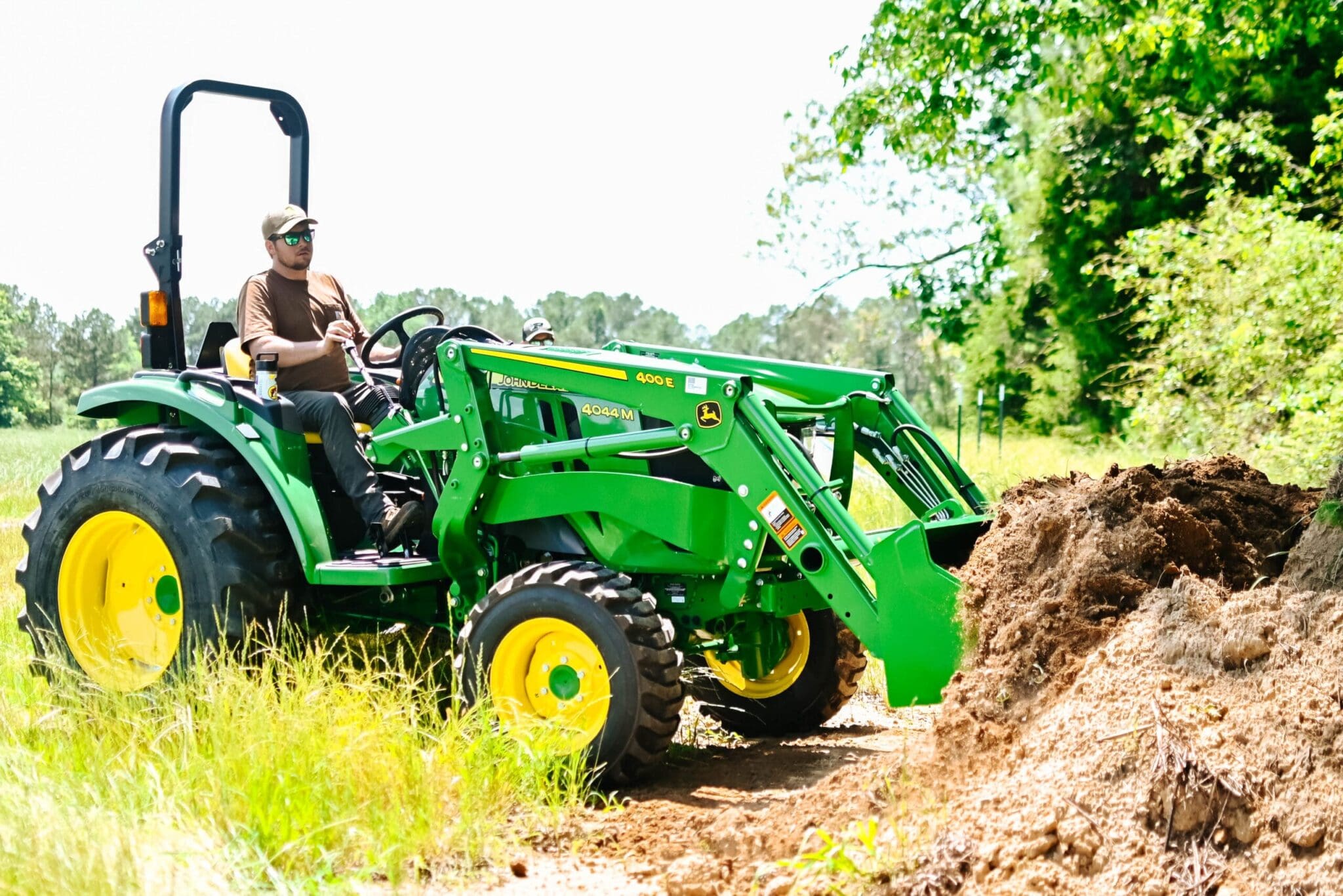 A man on a John Deere 4M tractor loader lifts a load of dirt