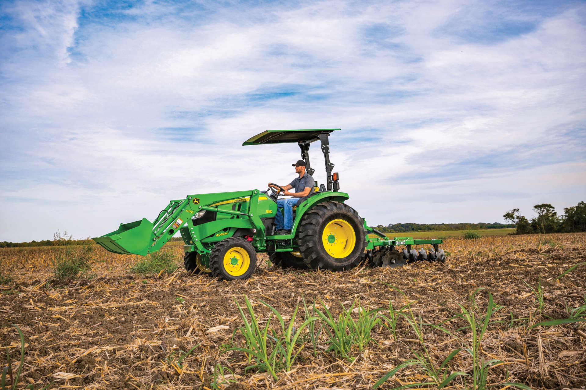A person works in a farm field with a John Deere Compact Utility Tractor