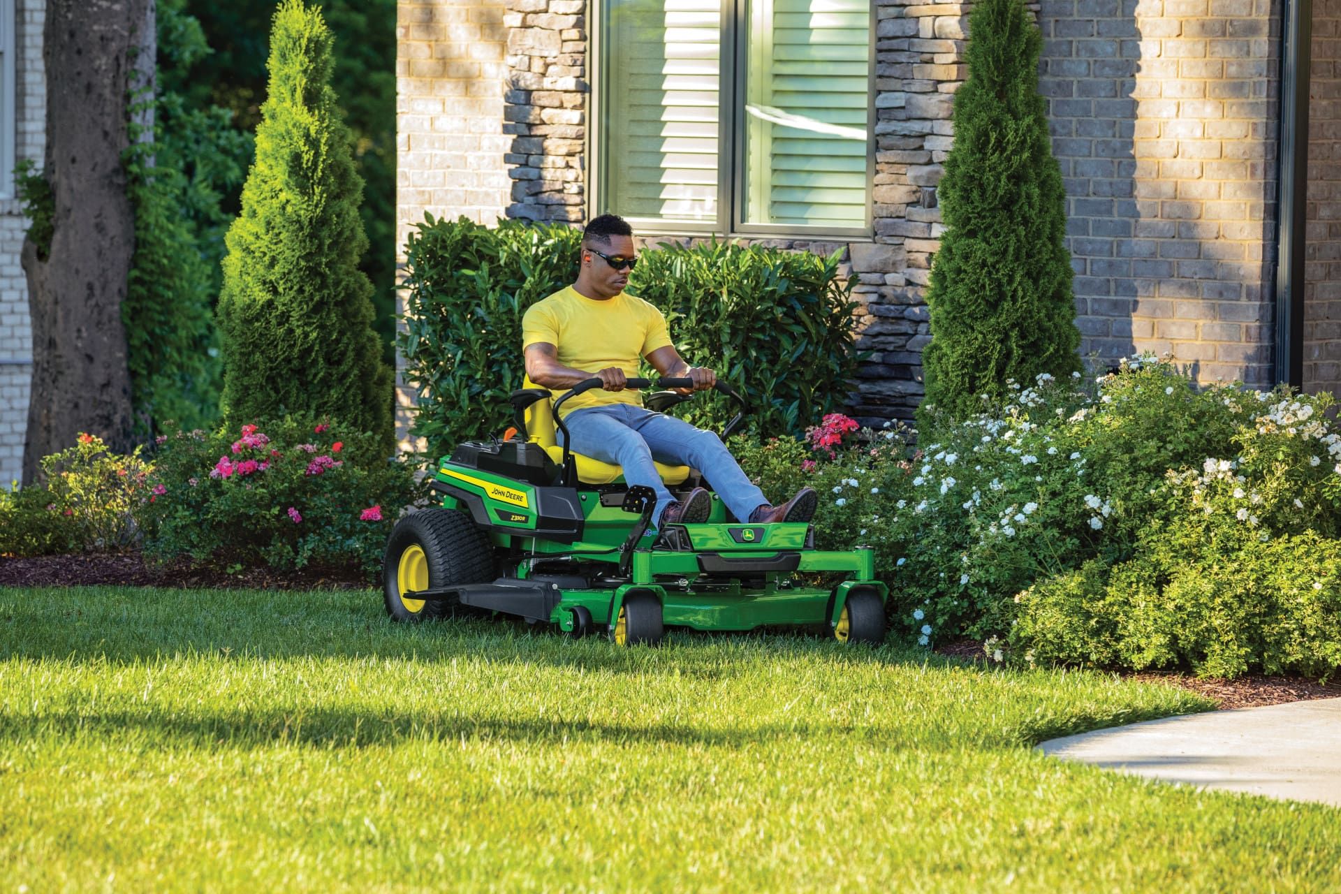 A man mows around flower beds with a Deere Z330R zero turn mower