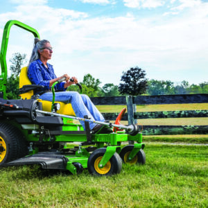 A woman mows along a fence with a Deere Z735M zero turn mower