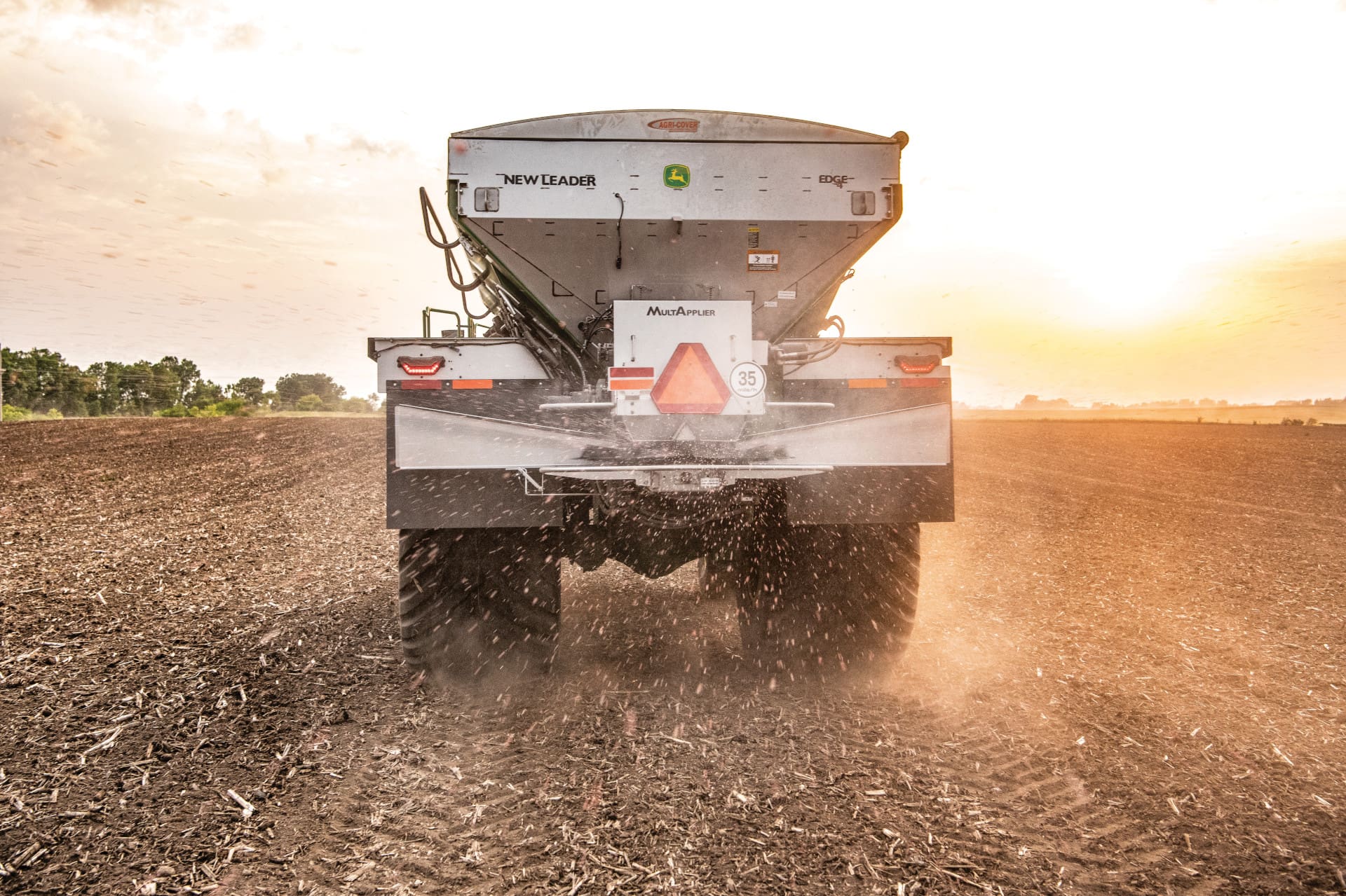 A John Deere dry spinner spreader in a field at sunset