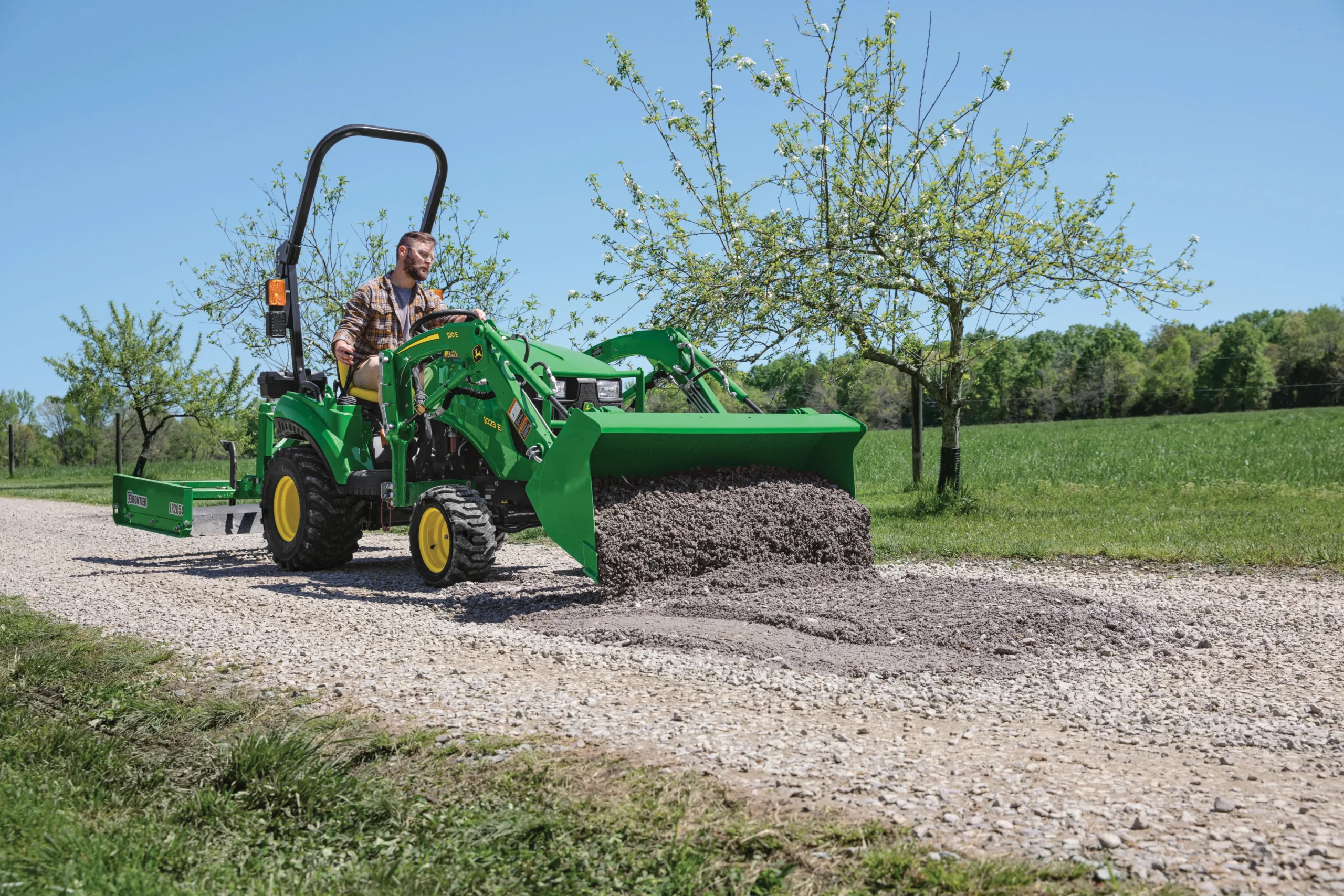 A man moves gravel on a road with a 1023E John Deere tractor