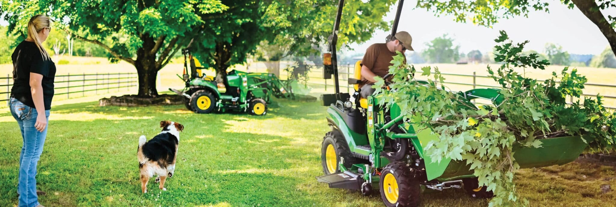 A person plays with a dog and a man moves tree limbs with a tractor