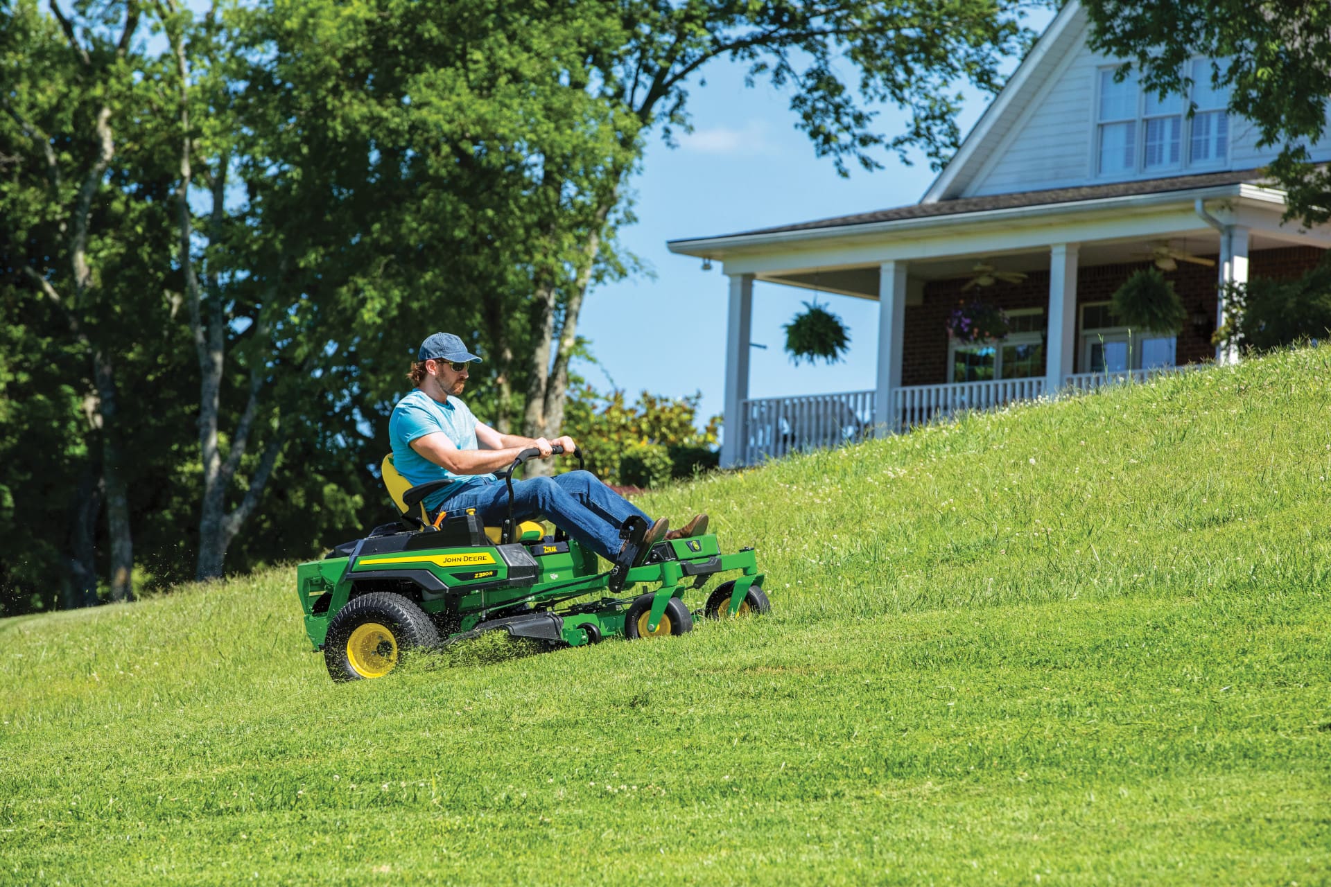 A person mows on a hill with a Deere Z300 series lawn mower